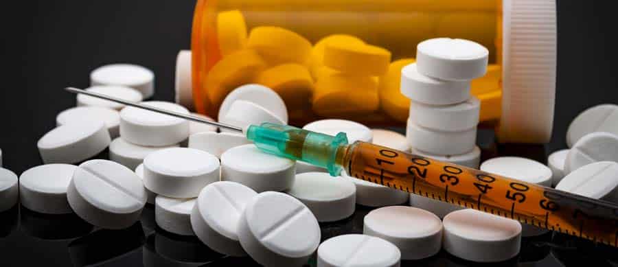 A syringe placed on top of scattered white prescription pills, emphasizing the illicit misuse and street-level abuse of prescription drugs.